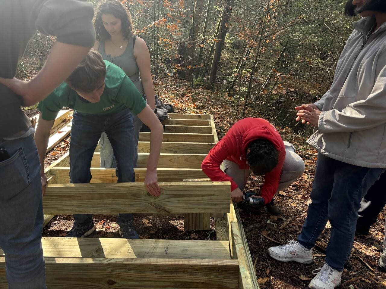 Alpha Phi Omega members building a new wooden campfire platform in the woods at Camp Jewell YMCA