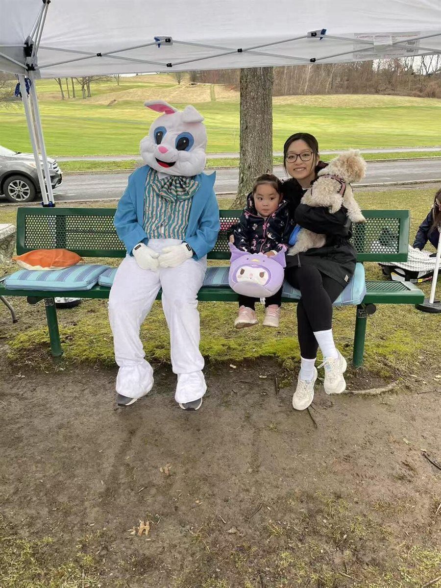 Armaan in an Easter Bunny costume next to a family on a bench at the Youth Service Day Easter celebration