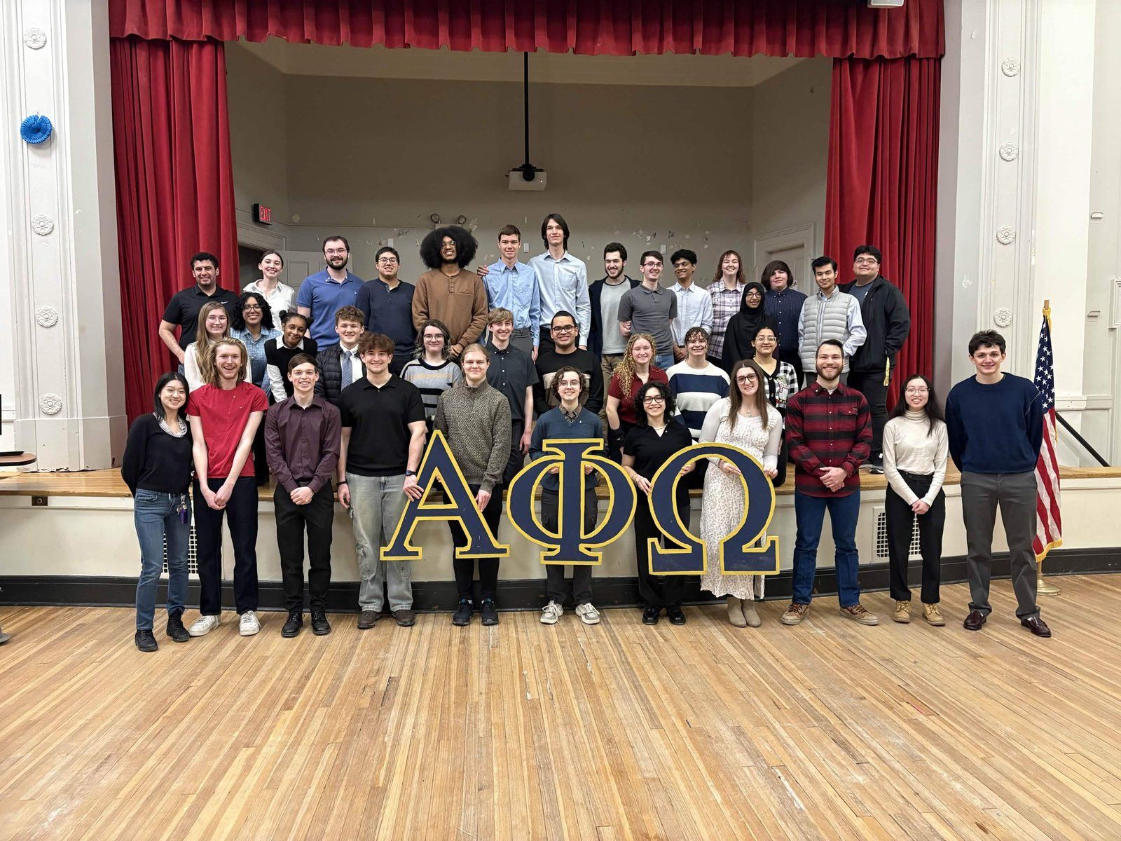 Alpha Phi Omega chapter group photo on stage during the New Member Ceremony, with large ΑΦΩ letters