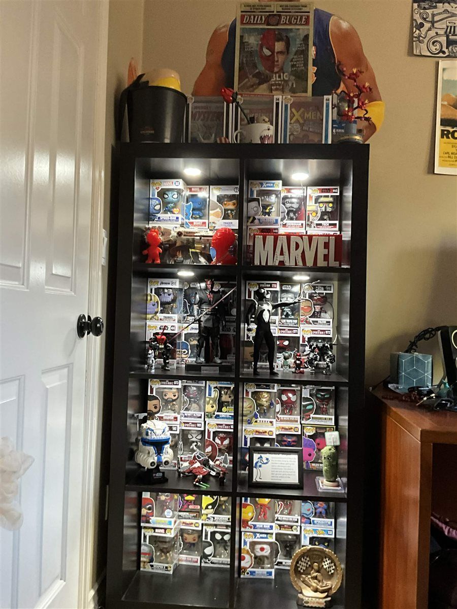 A tall display case full of Marvel and Star Wars Funko Pops, Hot Toys figures, and a Daily Bugle newspaper prop